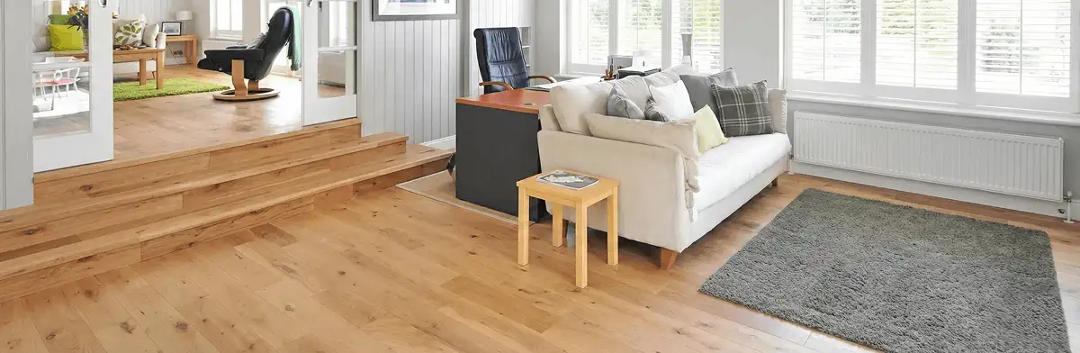 A modern living room with professionally installed laminate flooring, a beige sofa, a small side table, a gray rug, and large windows with white shutters in Miami, FL